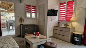 Uma sala de estar moderna com um sofá, uma mesa de centro com um vaso de flores, uma TV fixada na parede e uma área de jantar visível através de uma porta aberta.
