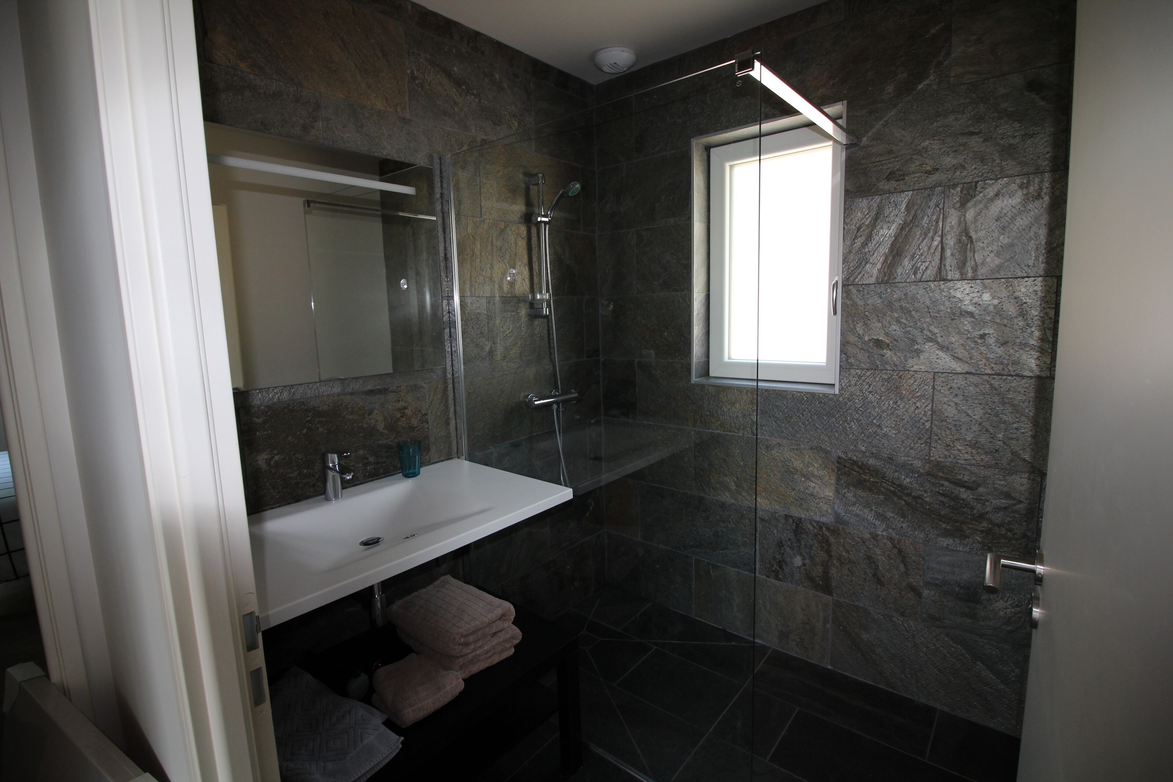 Une salle de bain moderne avec une douche à parois de verre, un lavabo blanc et un grand miroir.