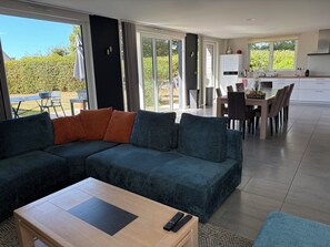 Una sala de estar moderna con un sofá modular, una mesa de centro de madera y un comedor con una mesa y sillas.