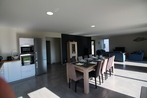 Een moderne keuken met inbouwapparatuur, een eethoek met een houten tafel en stoelen, en een zithoek met een bank en een televisie.