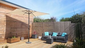 Un espace extérieur moderne, aménagé avec une terrasse en bois, un canapé doté de coussins bleus et un grand parasol.