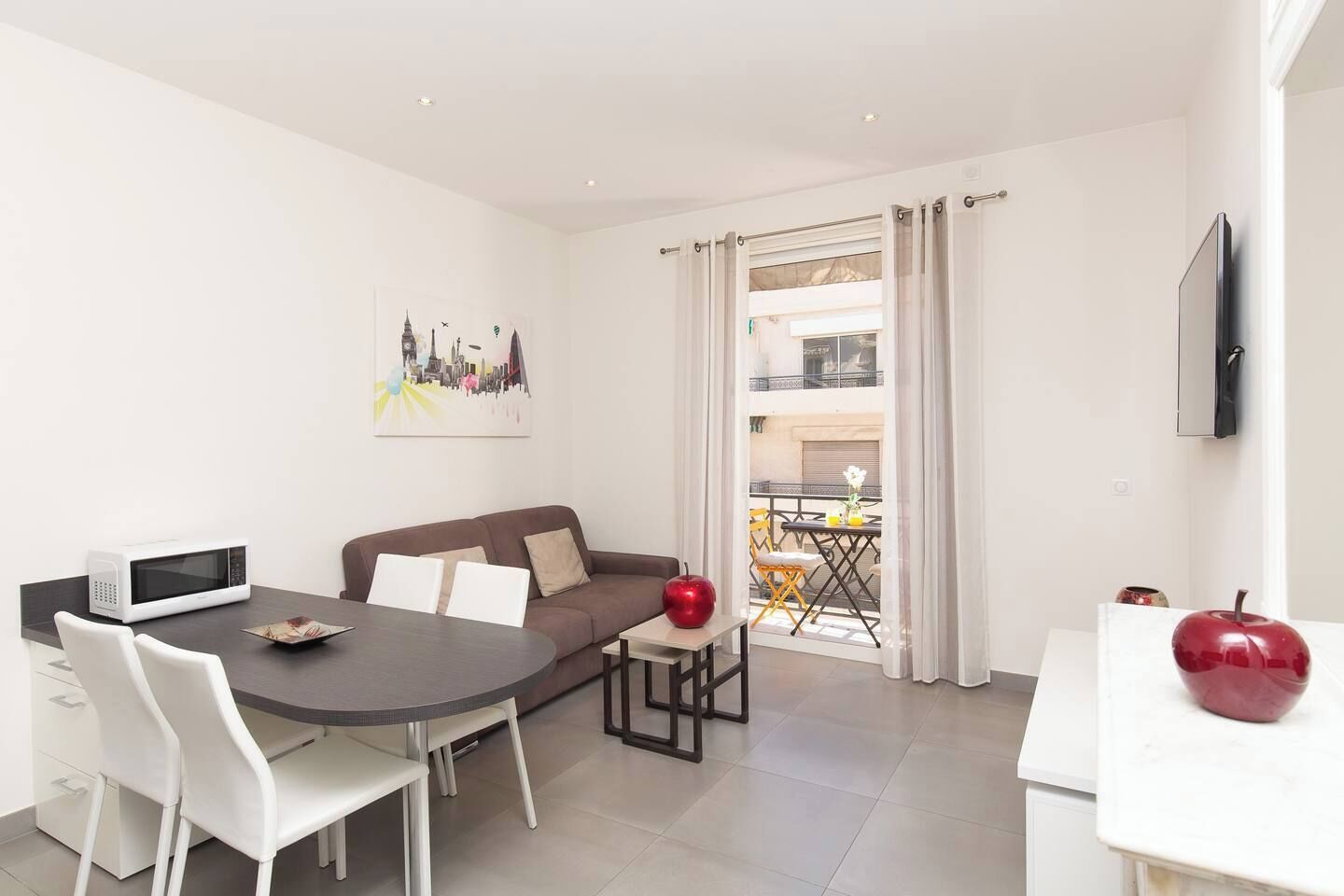 A modern living room with a dining area, a sofa, a TV, and a balcony with outdoor furniture.