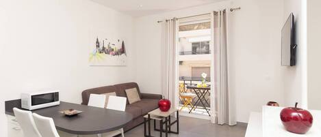 A modern living room with a dining area, a sofa, a TV, and a balcony with outdoor furniture.