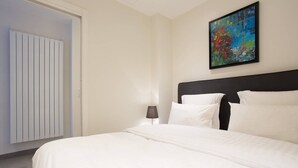 Ein Hotelzimmer mit einem großen Bett, einem schwarzen Kopfteil, einem farbenfrohen abstrakten Gemälde, einem weißen Heizkörper und einer Tür.