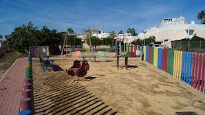Ein Spielplatz mit Schaukeln und einer Rutsche, umgeben von einem bunten Zaun.