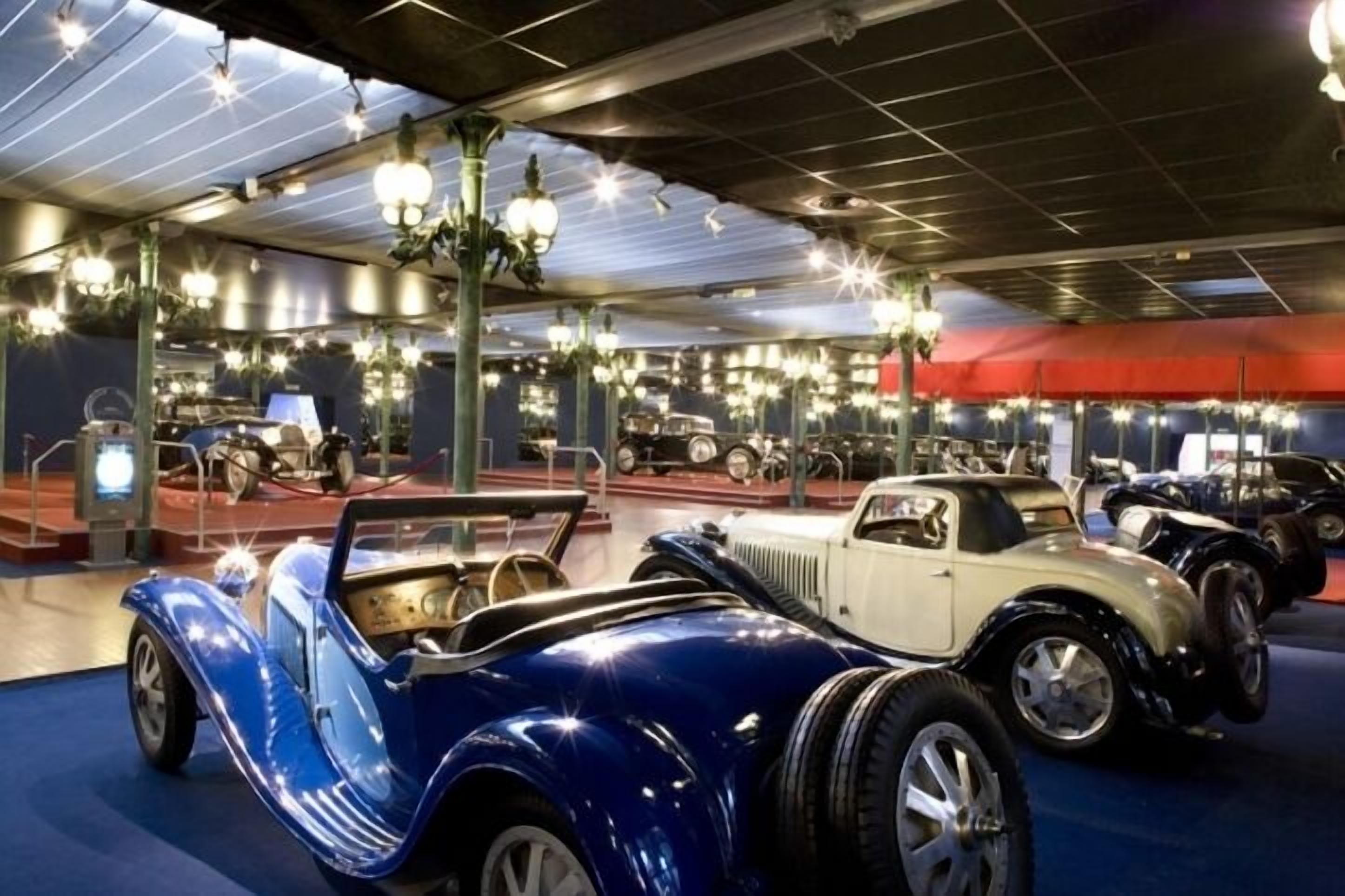 A museum with vintage cars on display, including a blue convertible and a white sedan.