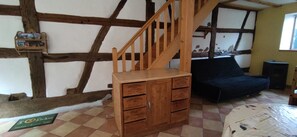 Quarto com escada de madeira, sofá preto e aparador de madeira com gavetas.