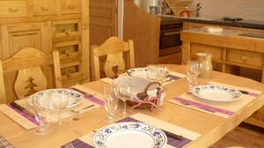 Une table de salle à manger en bois, mise avec des assiettes, des verres et des couverts, entourée de chaises en bois.