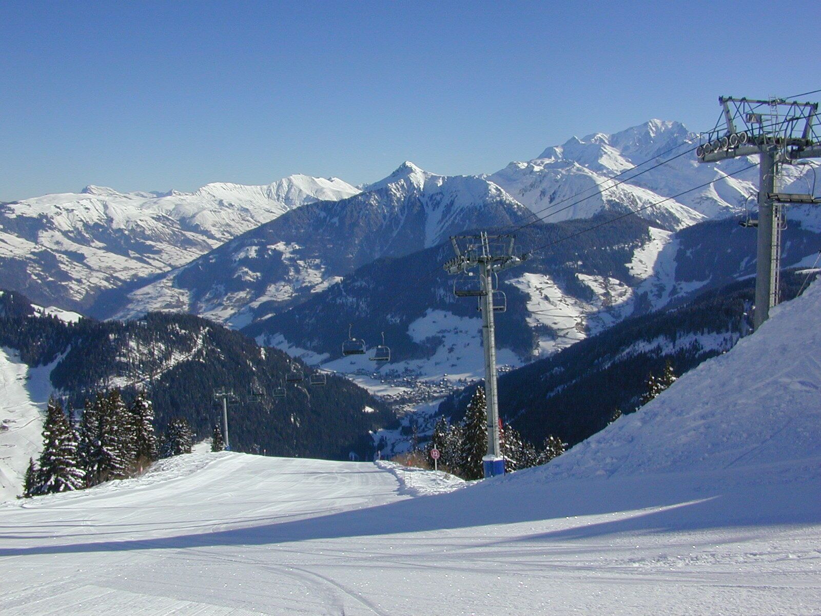 Une piste de ski avec un télésiège, des montagnes enneigées et un ciel dégagé.
