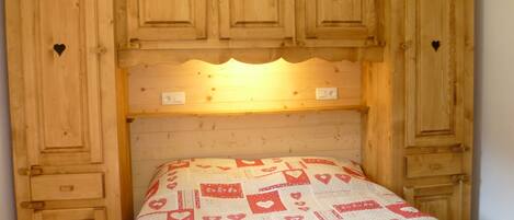 A bedroom with a wooden headboard, a bed with a patterned bedspread, and built-in wooden cabinets above the bed.