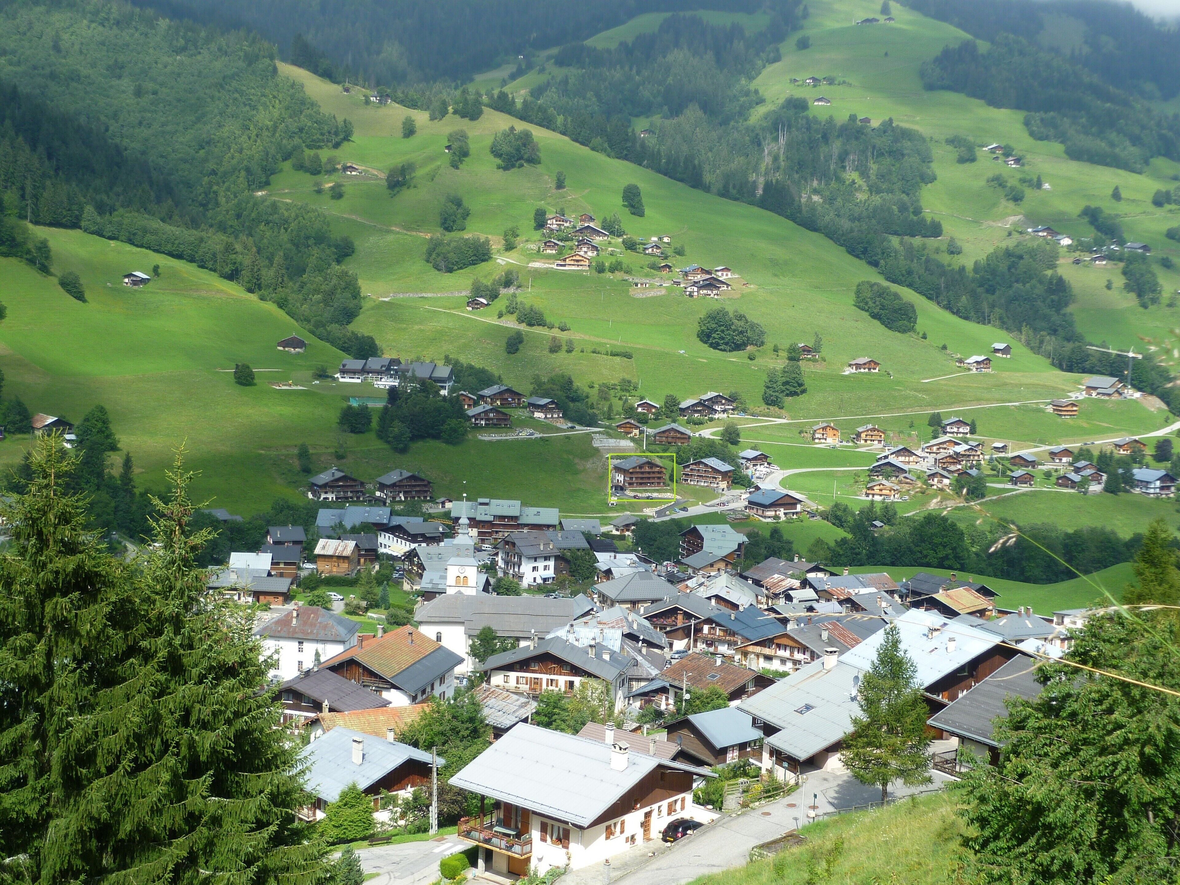A mountainous village with traditional wooden houses, a central square, and a church.