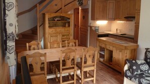 Une cuisine chaleureuse avec des meubles de rangement en bois, une table à manger et des chaises. Un escalier mène à l’étage supérieur.