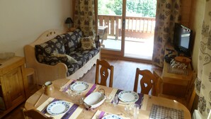 Un salon confortable avec un canapé, une table à manger dressée pour quatre personnes et un téléviseur posé sur un meuble.
