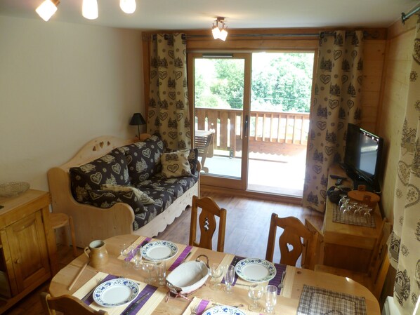 A cozy living room with a sofa, a dining table set for four, and a television on a stand.