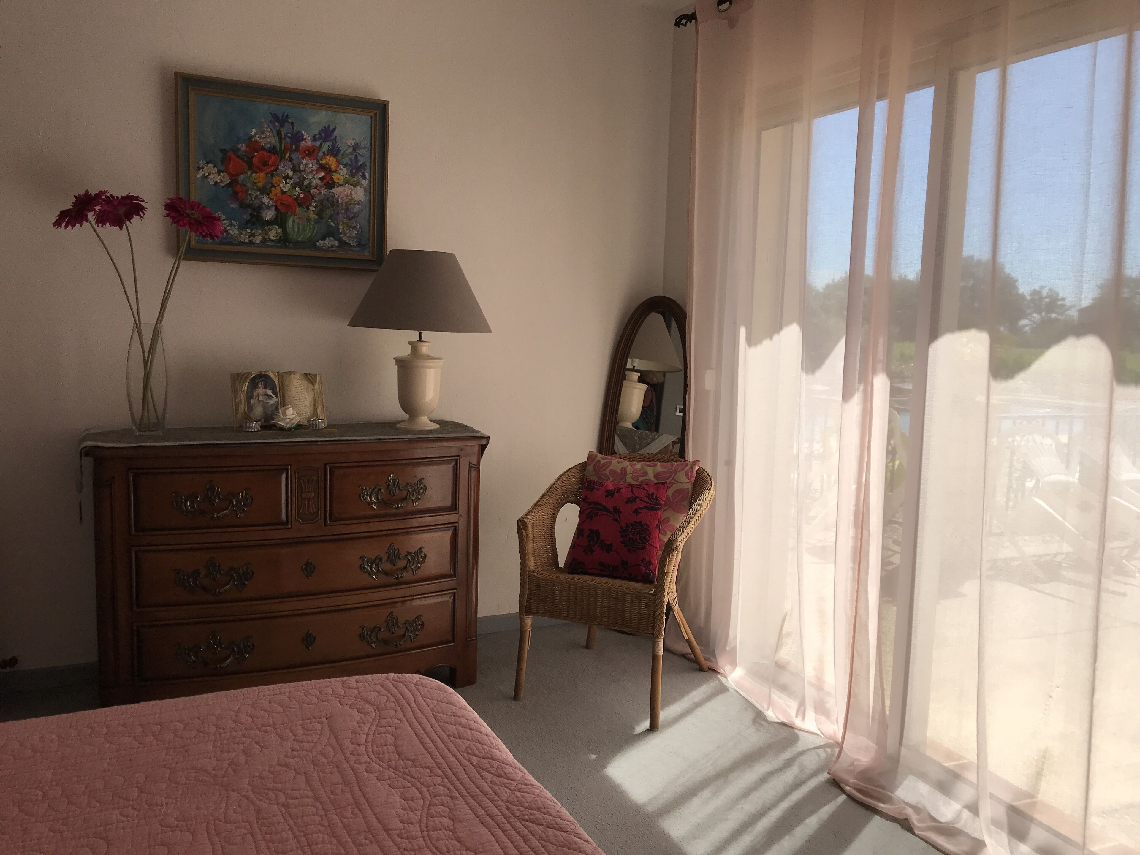 Een slaapkamer met een bed, een kaptafel, een spiegel en een bloemenstilleven.