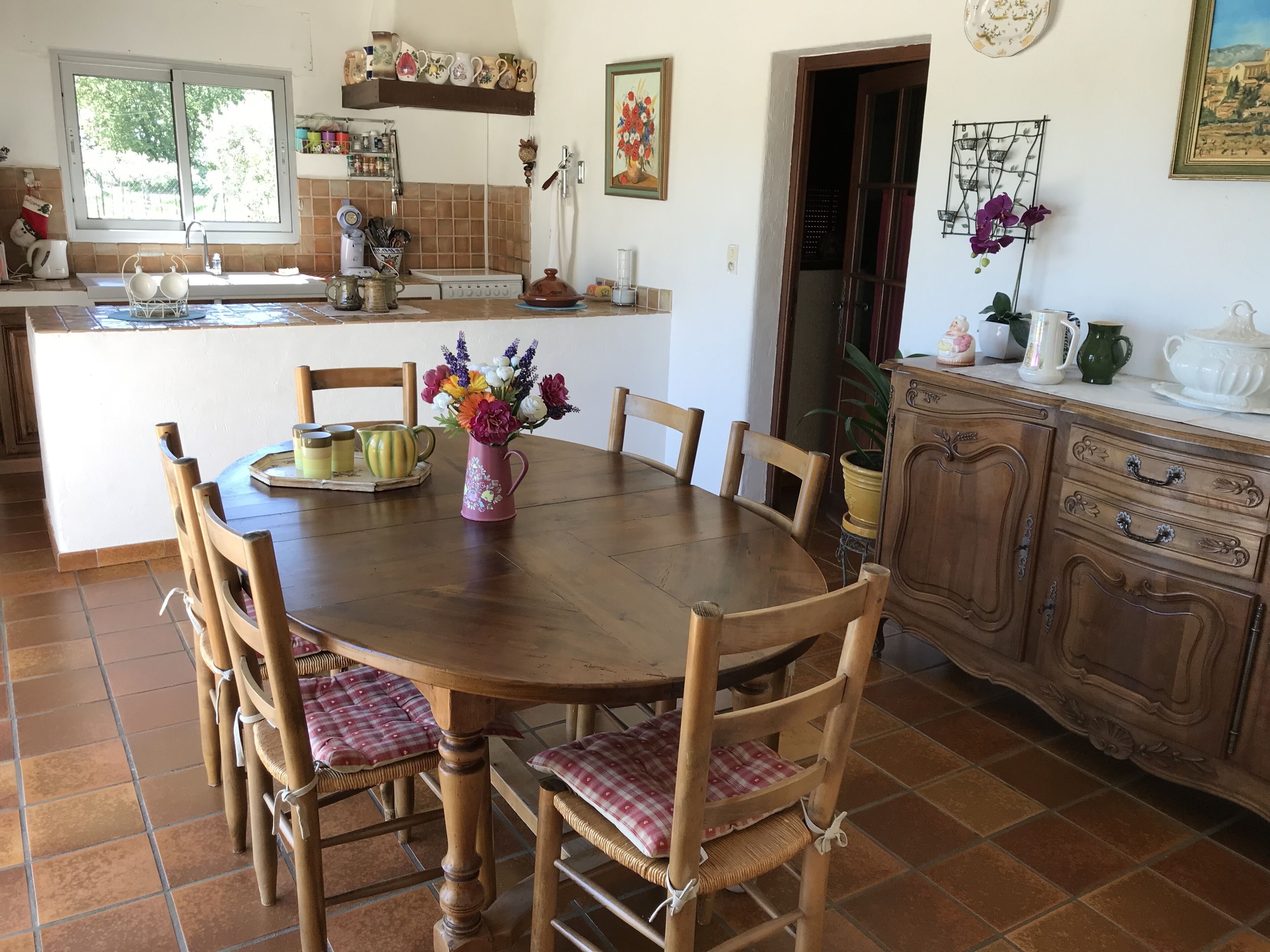Un coin repas avec une table en bois entourée de chaises, une cuisine en arrière-plan et un meuble avec des tiroirs.
