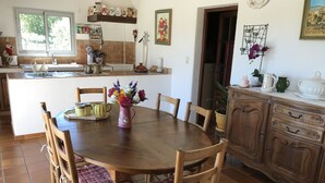 Un coin repas avec une table en bois entourée de chaises, une cuisine en arrière-plan et un meuble avec des tiroirs.