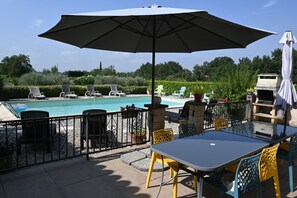 An outdoor patio with a pool, lounge chairs, and a table with chairs.