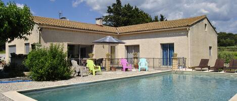 A swimming pool with lounge chairs and a building with a tiled roof.