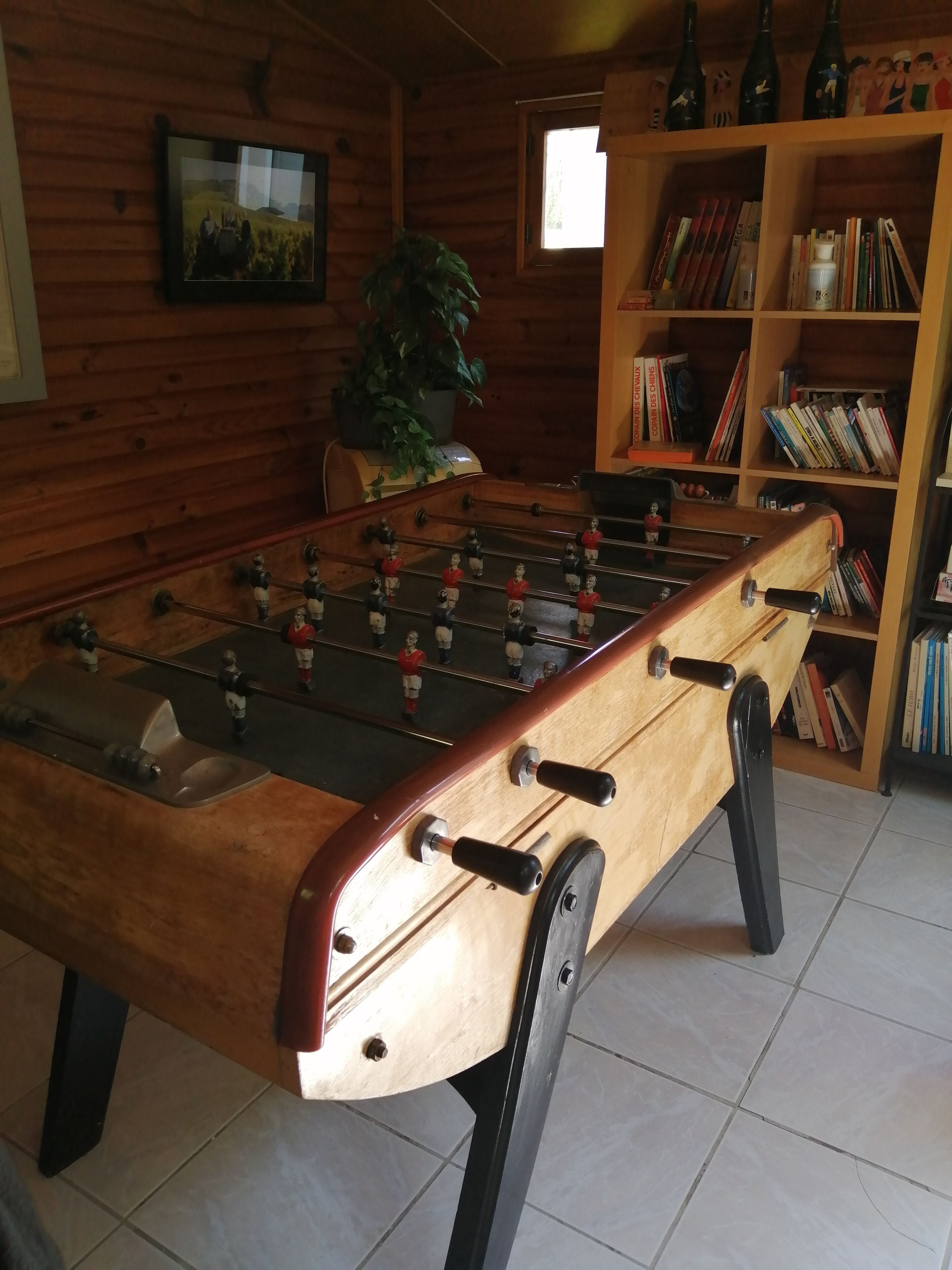 Ein Kicker aus Holz in einem Raum mit Bücherregal und Fenster.