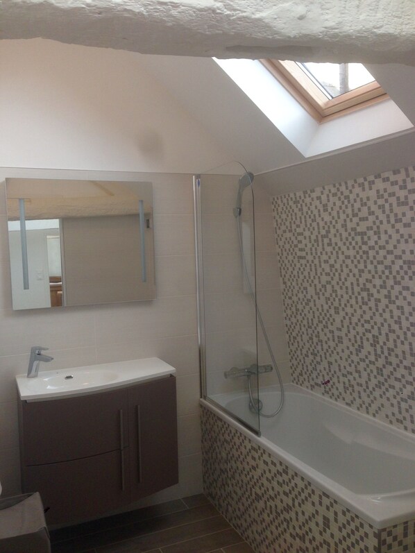 A bathroom with a skylight, a shower, a sink, and a tiled wall.