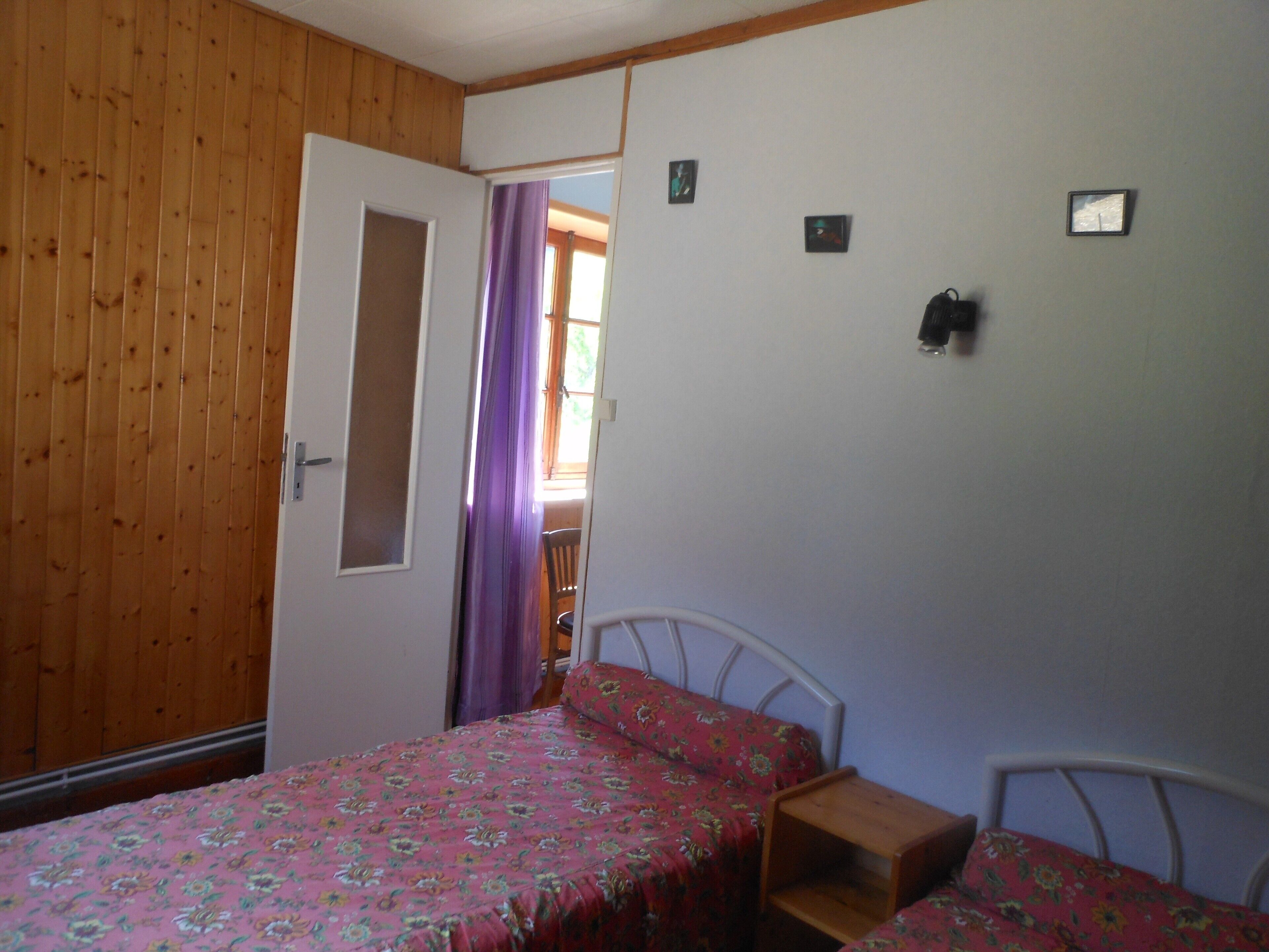 A bedroom with a wooden door, a bed with a floral bedspread, a nightstand, and a small table.