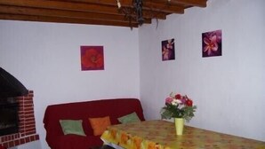 Ein gemütliches Zimmer mit einem roten Sofa, einer Holzbank und einem Tisch mit einer blumigen Tischdecke. An der Wand hängen zwei gerahmte Bilder.