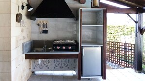 Une cuisine d’extérieur compacte, dotée d’une cuisinière à gaz, d’un réfrigérateur intégré et d’un porte-casseroles suspendu.