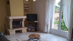 Un salon avec une cheminée, un téléviseur et une grande fenêtre avec des rideaux.
