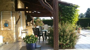Une terrasse extérieure agrémentée d’une pergola en bois, d’une table, de chaises et de plantes en pot.