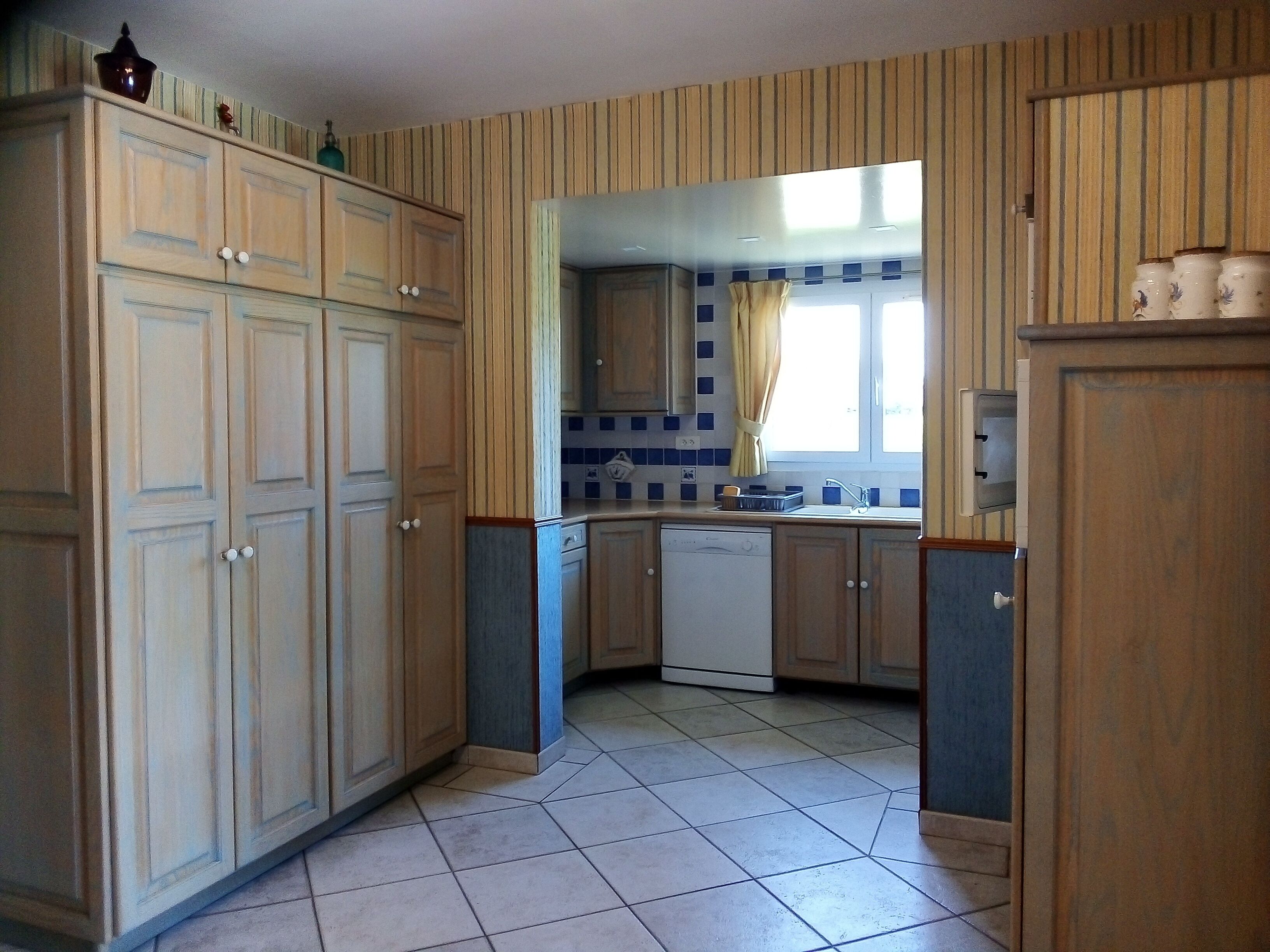 A kitchen with wooden cabinets, a dishwasher, and a window with curtains.