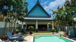 Un complexe hôtelier doté d’une piscine, de chaises longues et d’un aménagement paysager de style tropical.