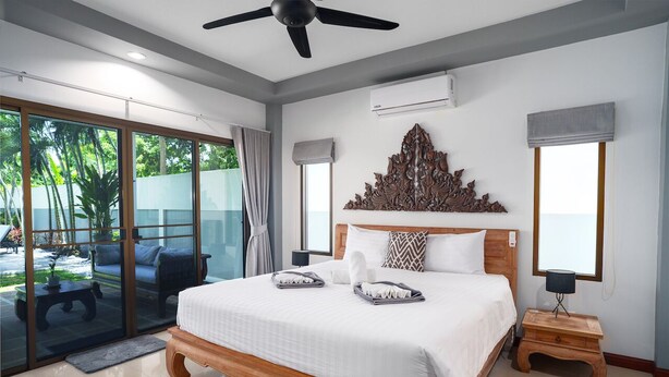 Une chambre dotée d’un grand lit, d’un ventilateur de plafond et offrant une vue sur l’extérieur grâce à une porte-fenêtre coulissante.