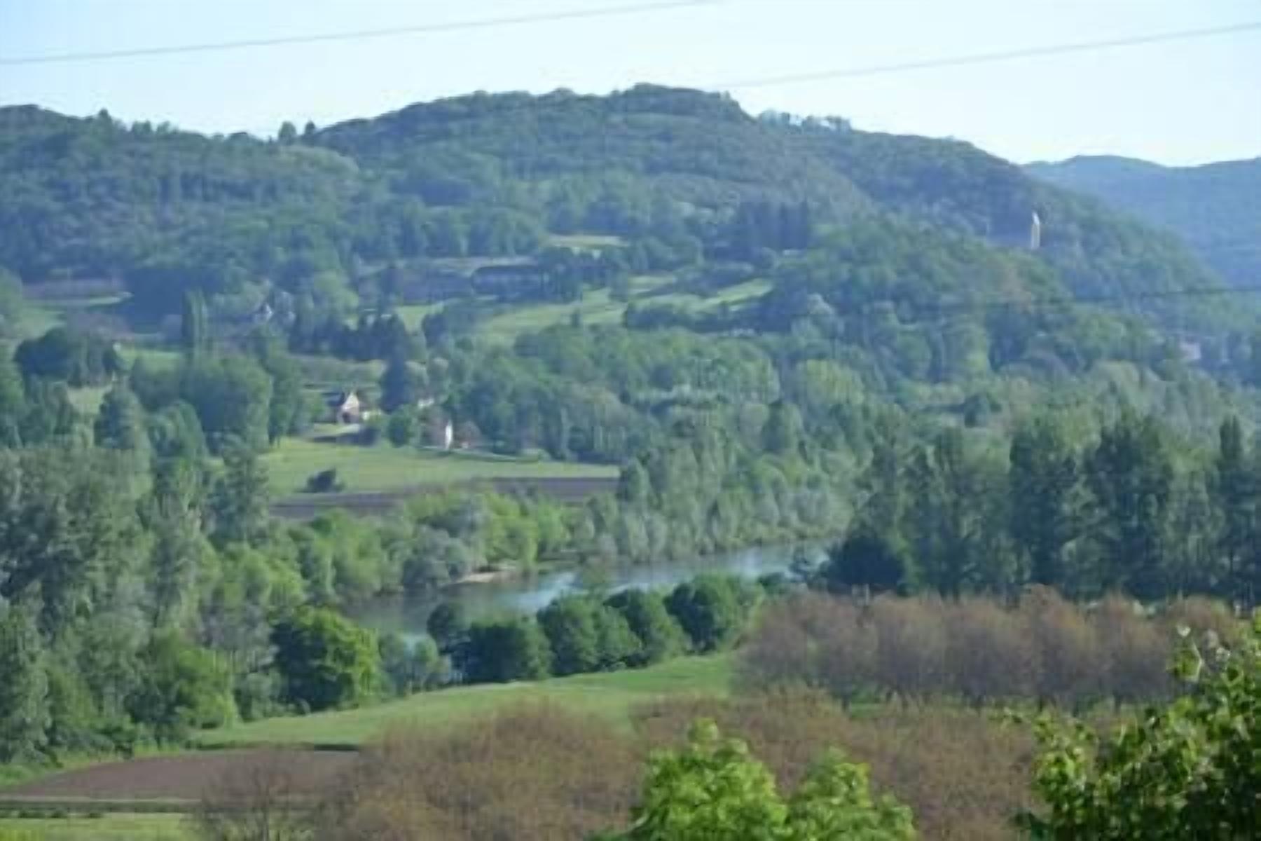 Un paysage rural caractérisé par des collines douces, une rivière et des maisons dispersées.