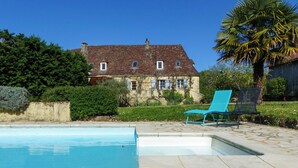 A swimming pool with a stone deck, a large house with a tiled roof, and a palm tree. - Le Bonheur dans notre pré - Castelnaud, charming gite in an old farm (Sainte-Mondane)