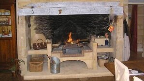 A stone fireplace with a fire burning, wooden shelves below, and a hanging decoration. - Le Bonheur dans notre pré - Castelnaud, charming gite in an old farm (Sainte-Mondane)