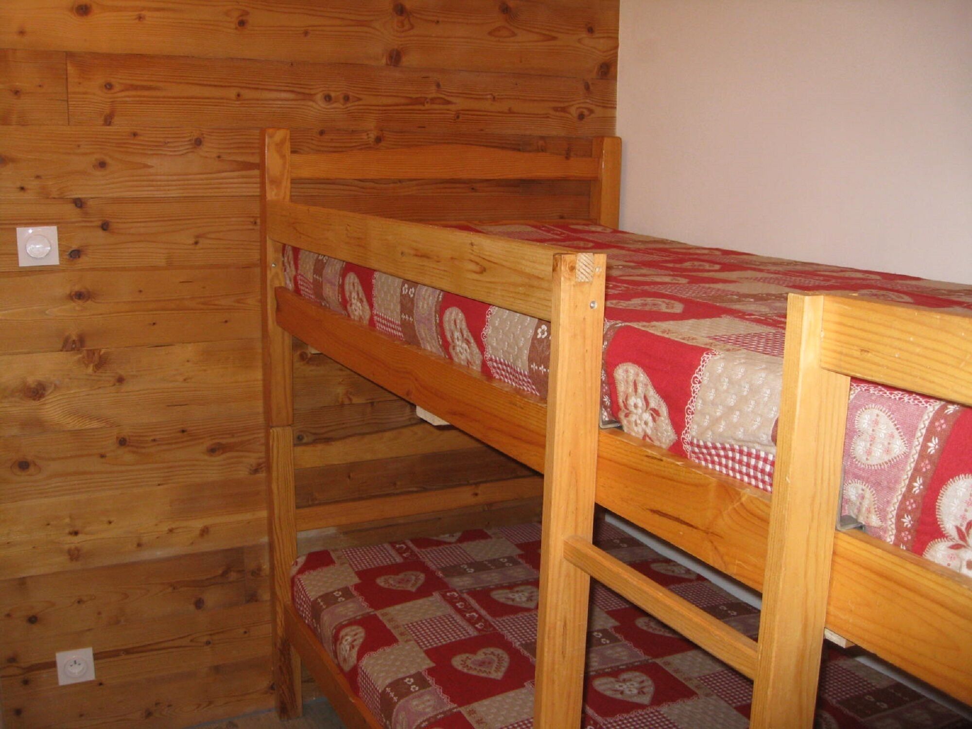 A bunk bed with a red and white patterned bedspread in a wooden room with a sloped ceiling.