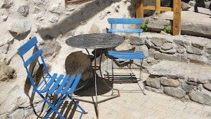 An outdoor seating area with a stone wall, a wooden window, and a wooden ladder.