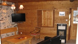 A wooden cabin interior with a stone wall, a television, a wooden table, a bench, and a fireplace.
