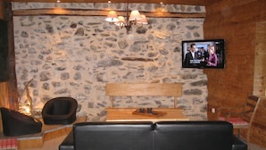 A cozy room with a stone wall, a wooden bench, a leather sofa, and a television mounted on the wall.