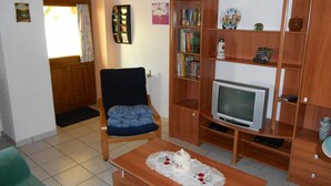 Ein Wohnzimmer mit einem Holzstuhl, einem Fernseher und einem Bücherregal.