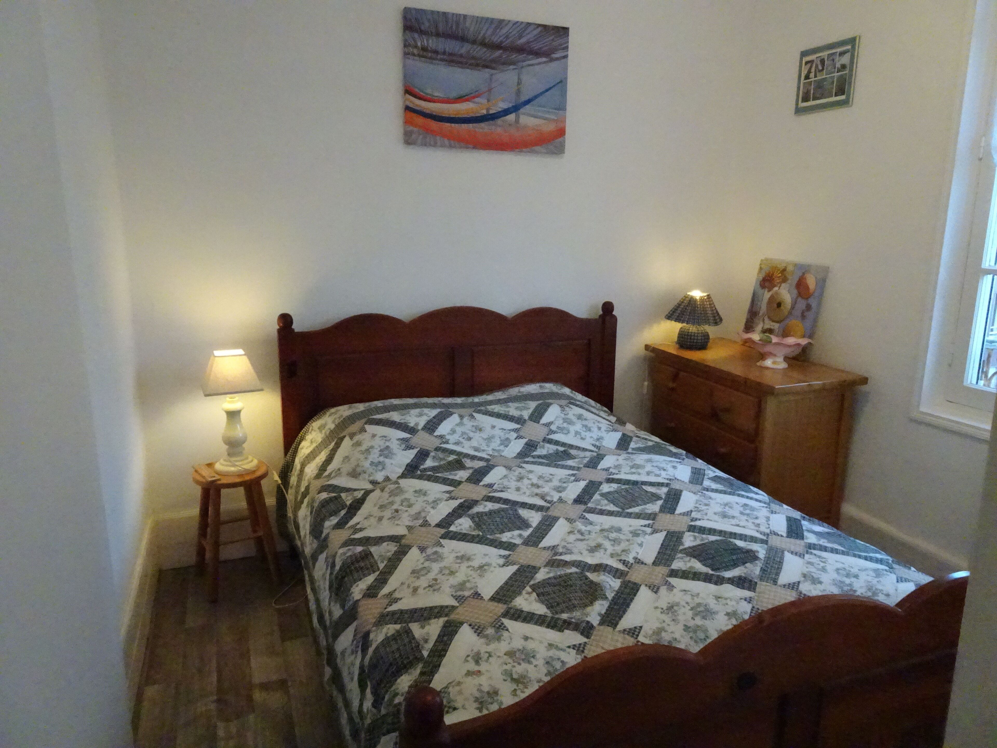 Une chambre à coucher avec un lit en bois, une table de chevet avec une lampe, une commode et un tableau accroché au mur.