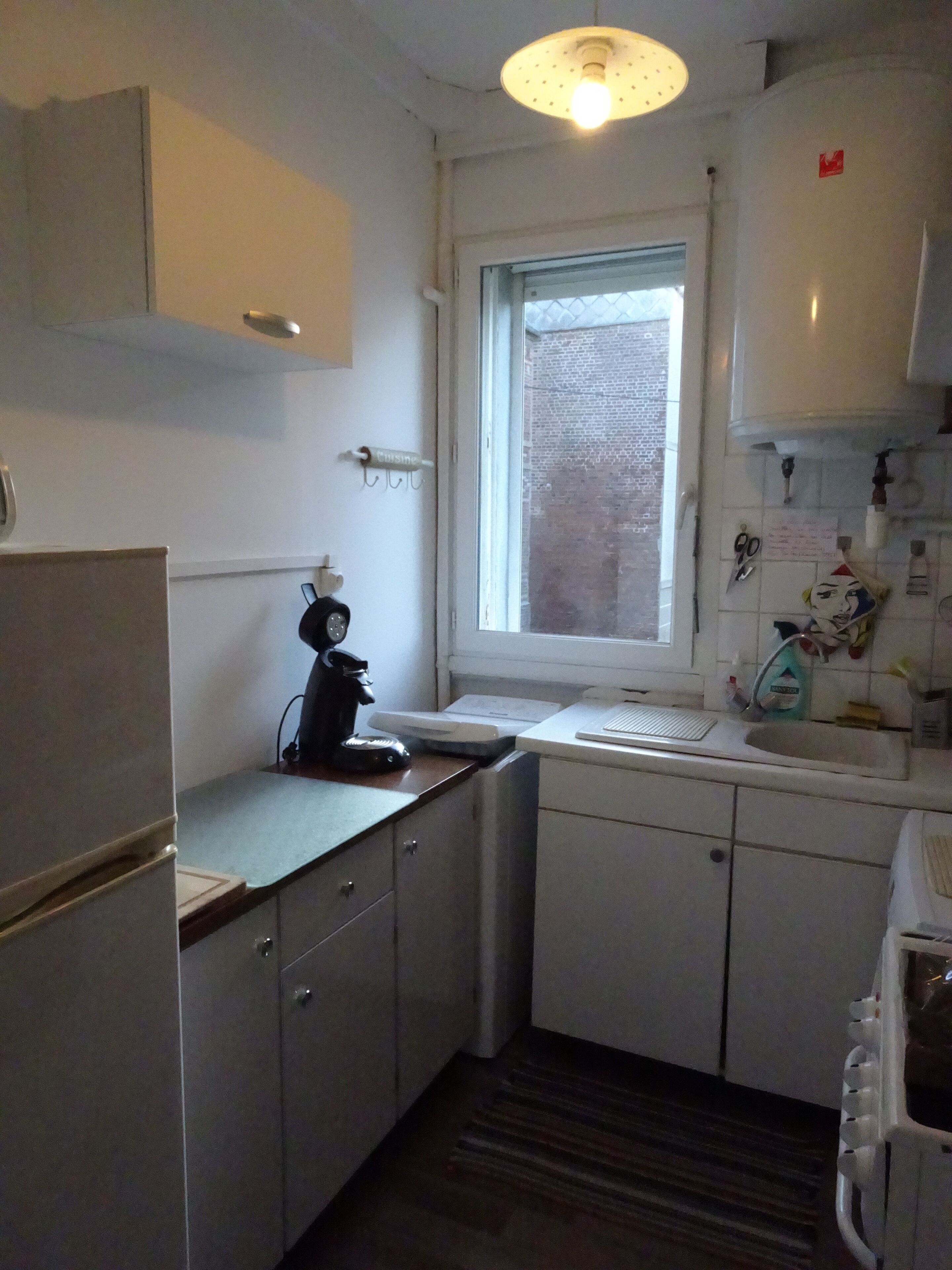 A compact kitchen with white cabinets, a built-in oven, a coffee maker, and a window with a view of a brick building.