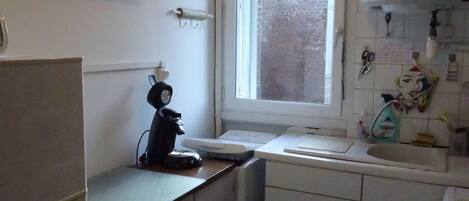 A compact kitchen with white cabinets, a built-in oven, a coffee maker, and a window with a view of a brick building.