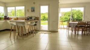 Una cucina moderna con mobili bianchi, un'area pranzo con sedie di legno e ampie finestre che si affacciano sul verde.