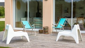 Una terrazza con due poltrone bianche e un cuscino blu, una grande porta scorrevole in vetro e una piccola pianta in vaso.