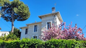 A stone building with a chimney, a large tree, and blooming pink flowers in the foreground. - Villa in Royan Park, 15 pers. - 200m from beach - 400m from shops/station. (Royan)