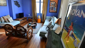 A living room with a blue wall, wooden furniture, a television, and a framed artwork. - Villa in Royan Park, 15 pers. - 200m from beach - 400m from shops/station. (Royan)