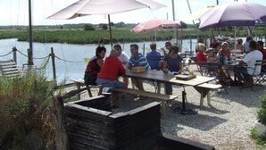 A group of people seated at tables under umbrellas by a riverside, with boats in the background. - Villa in Royan Park, 15 pers. - 200m from beach - 400m from shops/station. (Royan)