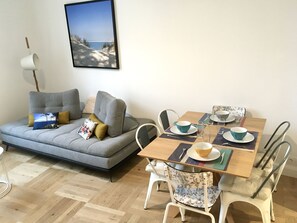 Un soggiorno con un divano grigio, un tavolo da pranzo in legno apparecchiato con piatti, tazze e posate, e un quadro appeso al muro.
